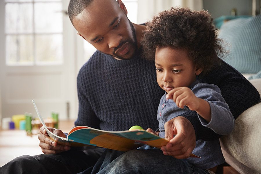 Personal Insurance - Father And Young Son Reading Book Together At Home